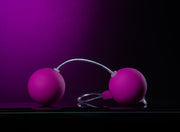 Two smooth, small, pink plastic Kegel balls connected by a pink cord with a loop at the bottom for easy retrieval. Additional images show alternate angles.